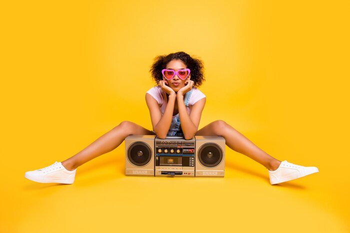 Poster  Portrait de sexy petite amie charmante dans les lunettes ayant boom box envoyant un baiser avec moue lèvres à la caméra isolé sur fond jaune. Concept de détente