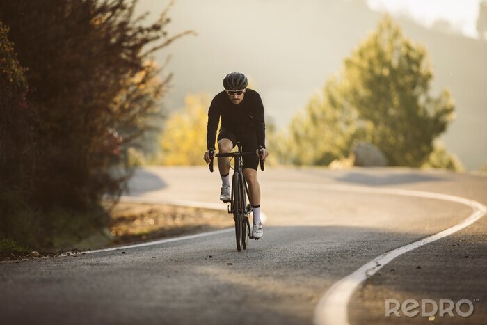 Poster  Professional road bicycle racer in action. Men cycling mountain road bike at sunset.