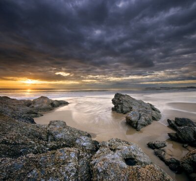 roches sur la plage au lever du soleil avec un ciel dramatique