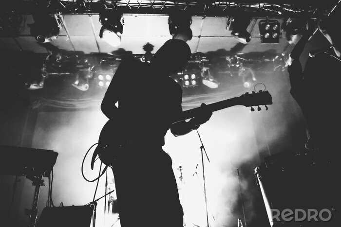 Poster  Silhouette de guitariste sur une scène dans une scène brillante s'allume. Noir et blanc