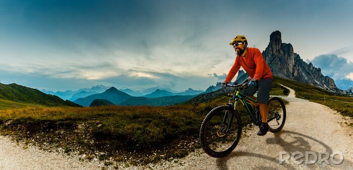 Poster  Single mountain bike rider on electric bike, e-mountainbike rides up mountain trail. Man riding on bike in Dolomites mountains landscape. Cycling e-mtb enduro trail track. Outdoor sport activity.