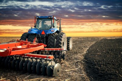 Tracteur labourant le champ sur fond de coucher de soleil