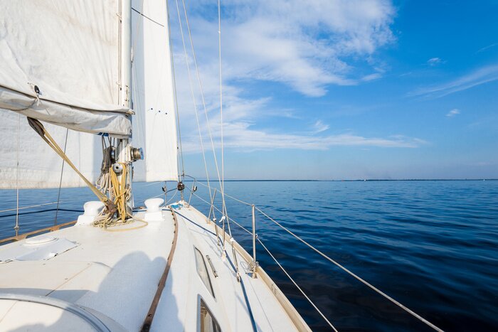 Poster  White sloop rigged yacht sailing near the coast of Maine, Southwest Harbor, USA. A view from the deck to the bow, mast and sails. Dark blue storm sky, sun rays through the clouds