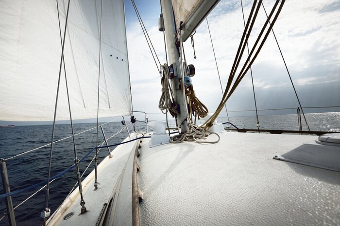 Poster  White yacht sailing on a sunny summer day. Close-up view from the deck to the bow, mast and sails. Waves and water splashes. Clear blue sky. Gulf of Finland