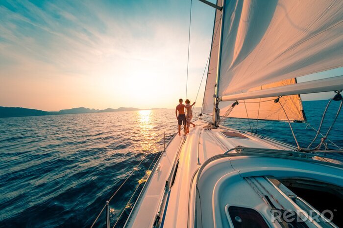 Poster  Young couple enjoys sailing in the tropical sea at sunset on their yacht.