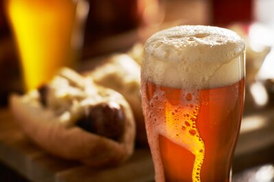 Bière IPA avec la tête écumeuse débordante dans la tasse servi avec bratwursts