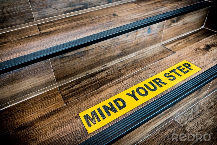 Sticker  Faites attention à votre signe adhésif étape collé sur un escalier en bois. Concepts d'avertissement, d'abstraction ou d'architecture intérieure