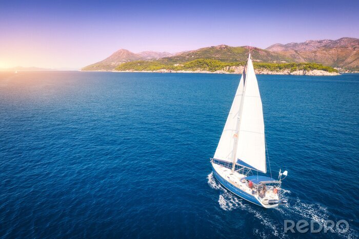 Tableau  Aerial view of beautiful white sailboat in blue sea at bright sunny summer evening. Adriatic sea in Croatia. Landscape with yacht, mountains, transparent blue water, sky at sunset. Top view of boat