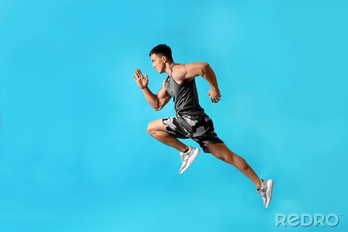 Tableau  Athletic young man running on light blue background, side view