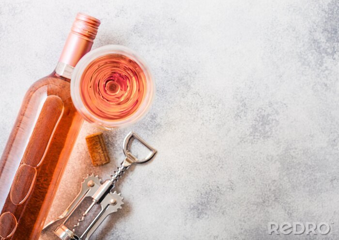 Tableau  Bottle and glasses of pink rose wine with cork and corkscrew opener on stone kitchen table background. Top view. Space for text