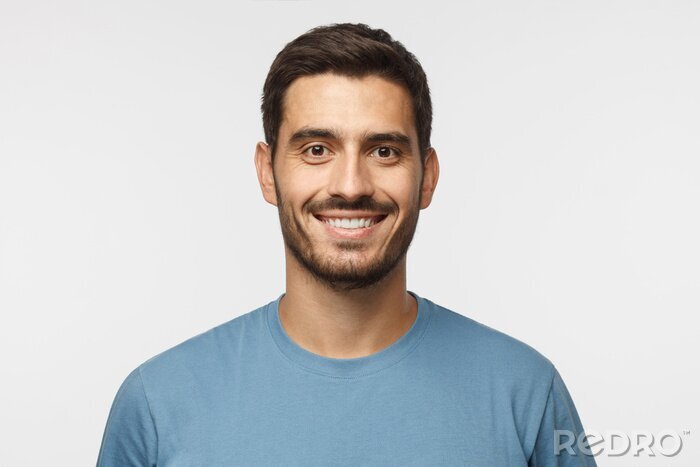Tableau  Bouchent portrait de jeune beau mec souriant en t-shirt bleu isolé sur fond gris