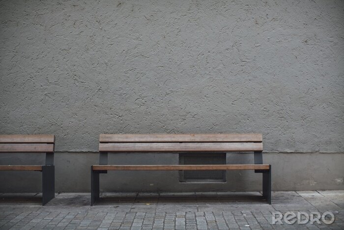 Tableau  Closeup shot of wooden benches against a grey stone wall in an empty street