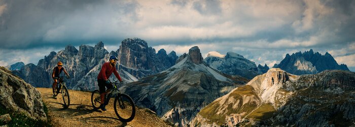 Tableau  Cycling outdoor adventure in Dolomites. Cycling woman and man  on electric mountain bikes in Dolomites landscape. Couple cycling MTB enduro trail track. Outdoor sport activity.