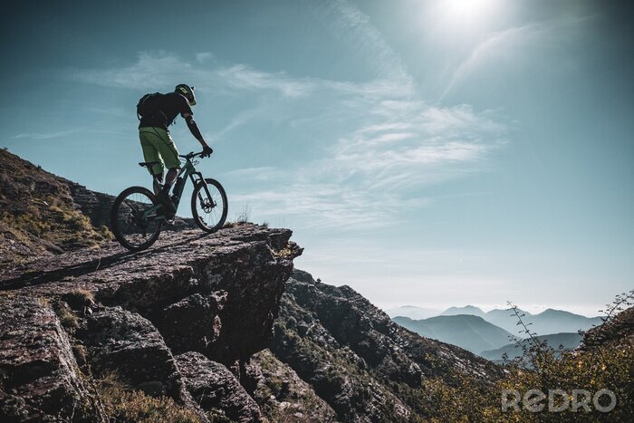 Tableau  cycliste de montagne sur un grand rocher au fond des Alpes avec des couches de soleil et de montagne derrière