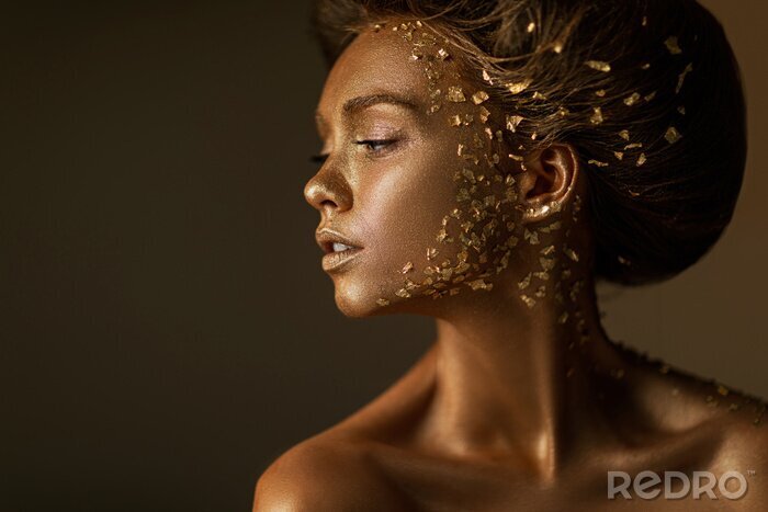 Tableau  Fashion art portrait of model girl with holiday golden shiny professional makeup. beaty woman with gold metallic body and hair on dark background. Gold glowing skin. copy space