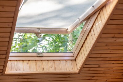 Tableau  Fenêtre de toit ouverte avec stores ou rideaux dans le grenier de la maison en bois. Chambre avec plafond incliné en matériaux écologiques naturels et vue sur le parc par une fenêtre ouverte. Maison r
