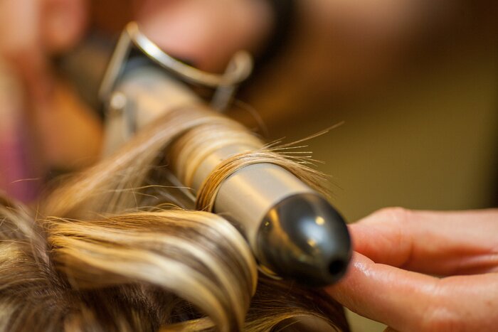 Tableau  Hairdresser curling a blond woman's hair in professional hairdressing salon or barbershop , seen from behind the customer, unrecognizable.