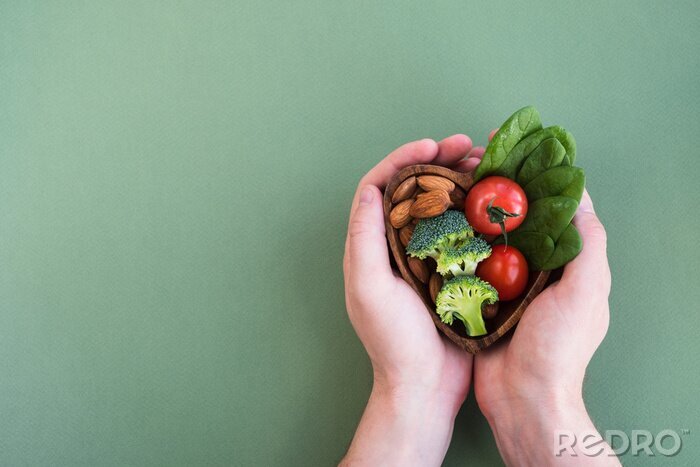 Tableau  Healthy food for heart on green background. Man hands hold plate with vegetables, spinach and nuts. Diet, superfood and health concept. Top view, flat lay, copy space