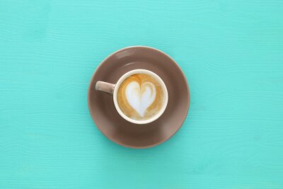Tableau  image de tasse à café avec mousse de forme de coeur sur la table en bois bleue.