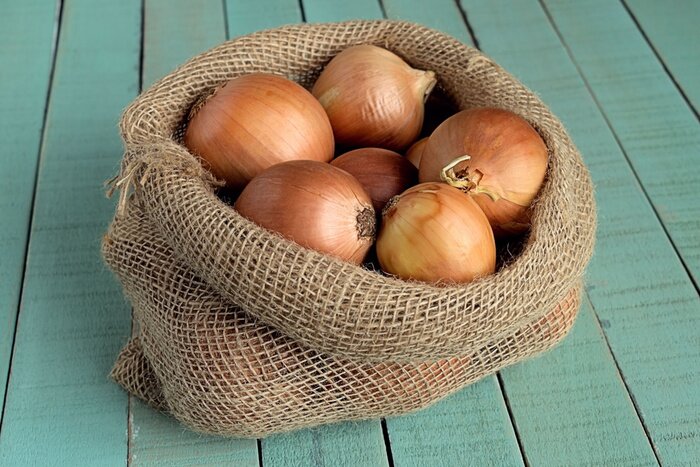 Tableau  Oignons. Sachet d'oignons sur fond de bois.