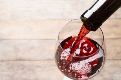 Tableau  Pouring red wine from bottle into glass on blurred background, closeup. Space for text