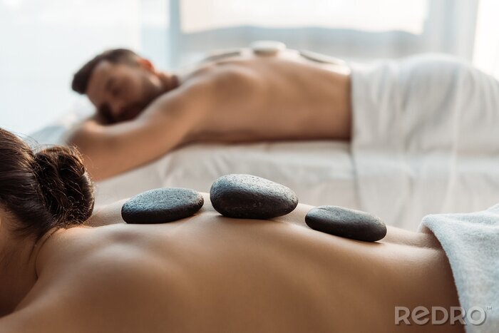 Tableau  selective focus of woman having stone massage near man in spa center