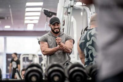 Tableau  strong muscle bearded caucasian athlete man holding his wrist with hand during sport training injury with grimace of pain on his face indoor gym