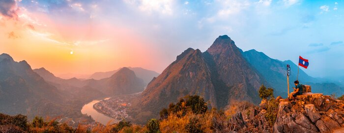 Tableau  Sunset panoramic view of couple of trekkers sitting on a rock on top of Nong Khiaw View Point with beautiful mountain and Nam Ou river in background, Luang Prabang Province, Northern Laos.