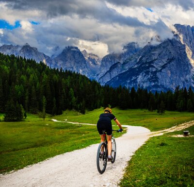 Tableau  Tourist cycling in Cortina d'Ampezzo, stunning rocky mountains on the background. Woman riding MTB enduro flow trail. South Tyrol province of Italy, Dolomites.