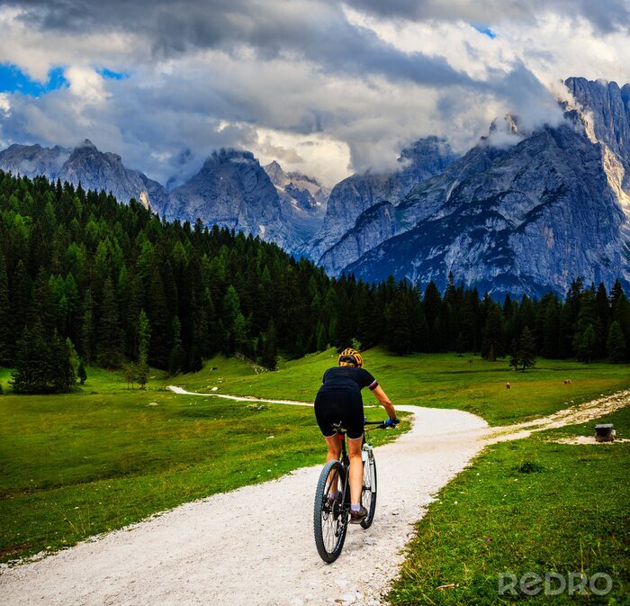 Tableau  Tourist cycling in Cortina d'Ampezzo, stunning rocky mountains on the background. Woman riding MTB enduro flow trail. South Tyrol province of Italy, Dolomites.