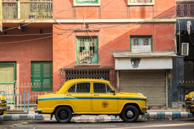 Tableau  Un taxi de taxi jaune de l'ambassadeur est garé dans la rue sous une maison de couleur rouge à Kolcata, en Inde