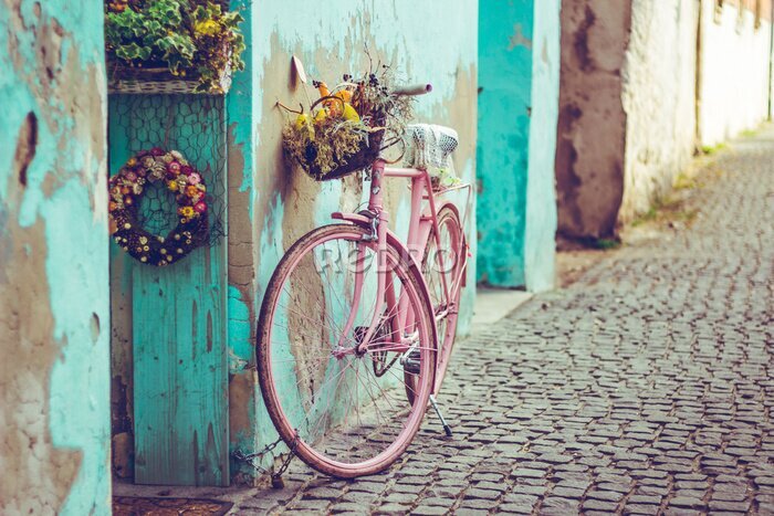 Tableau  Vélo vintage rose avec panier rempli de fleurs à côté d'un vieux bâtiment cyan en Espagne