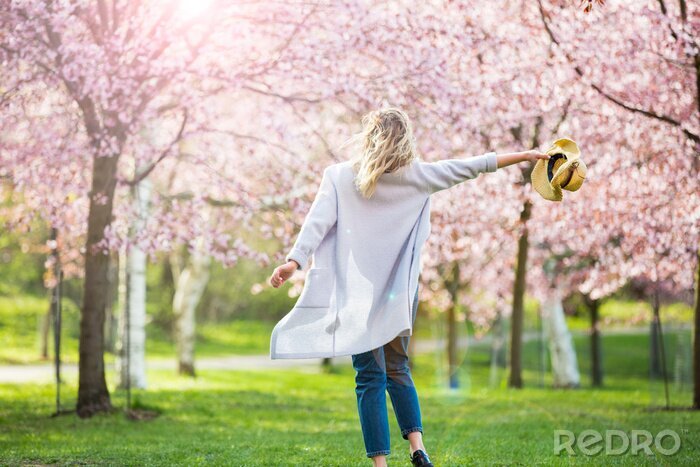 Tableau  Young woman enjoying the nature in spring. Dancing, running and whirling in beautiful park with cherry trees in bloom. Happiness concept